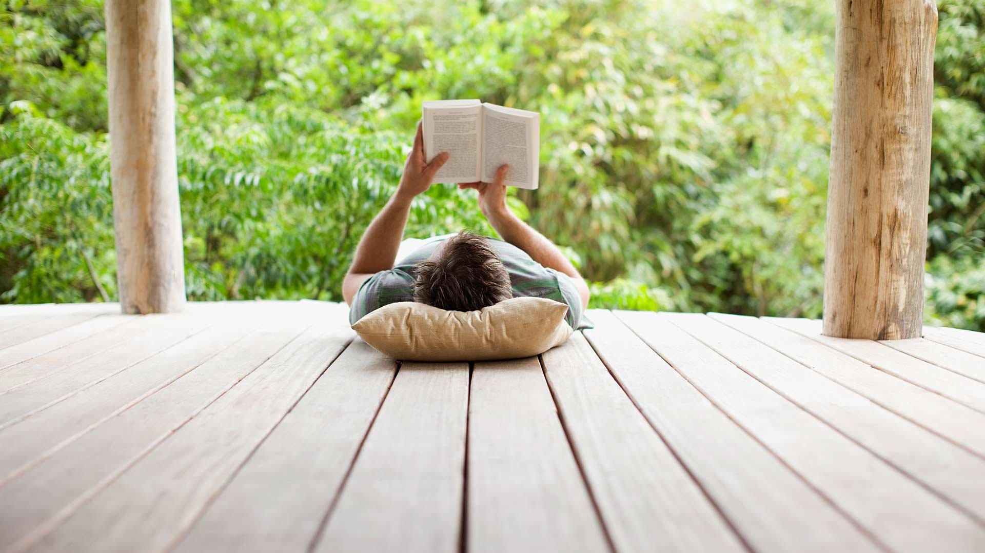 Mann entspannt mit Buch auf Terrasse
